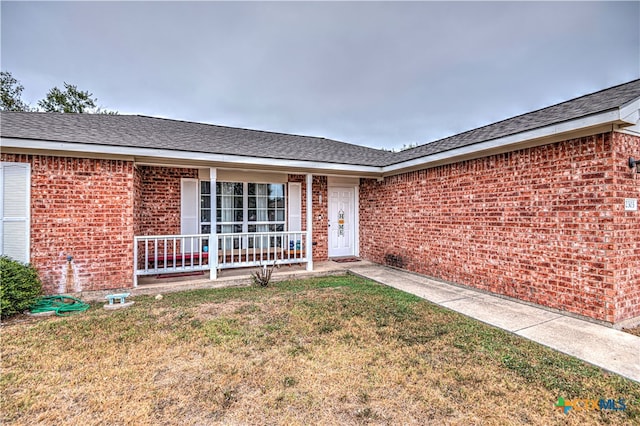 doorway to property featuring a porch and a lawn