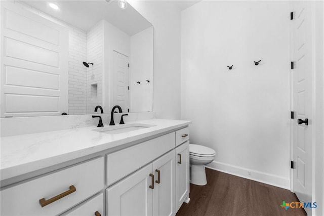 full bathroom featuring toilet, vanity, wood finished floors, tiled shower, and baseboards