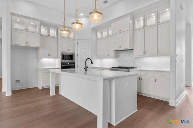 kitchen with wall oven, a sink, wood finished floors, light countertops, and stainless steel microwave