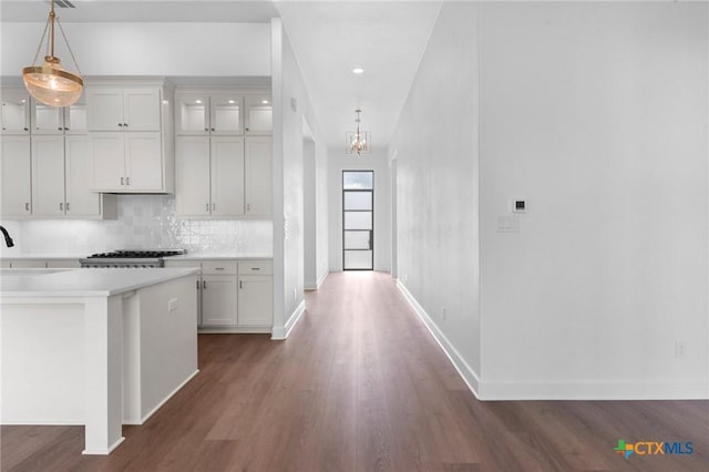 kitchen featuring decorative light fixtures, dark wood finished floors, light countertops, decorative backsplash, and baseboards