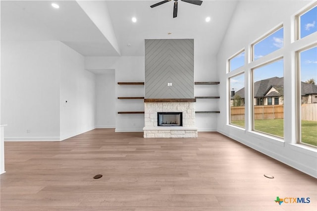 unfurnished living room featuring light wood finished floors, a high ceiling, a ceiling fan, a stone fireplace, and baseboards