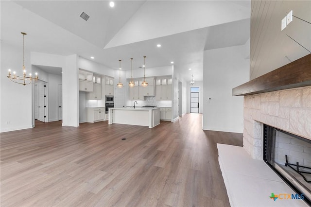 unfurnished living room featuring a fireplace with raised hearth, high vaulted ceiling, a notable chandelier, a sink, and wood finished floors