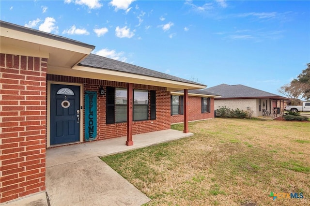 doorway to property with brick siding, a shingled roof, and a yard