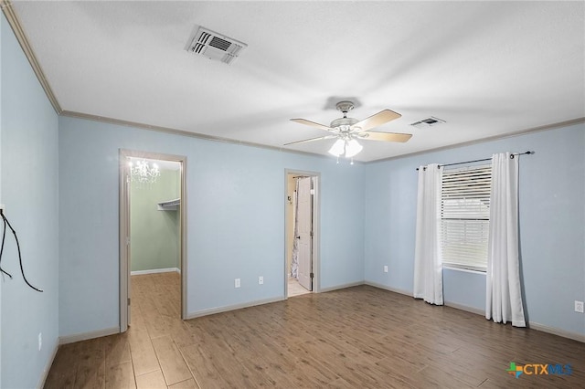 empty room featuring ceiling fan, visible vents, wood finished floors, baseboards, and ornamental molding