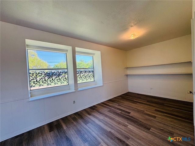 unfurnished room featuring a textured ceiling, dark wood-style flooring, and wainscoting