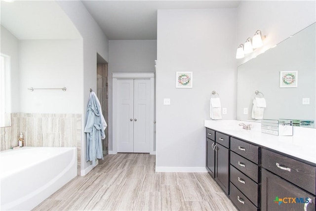 bathroom with wood finished floors, a garden tub, vanity, and baseboards