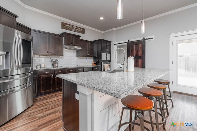 kitchen featuring a barn door, tasteful backsplash, stainless steel fridge with ice dispenser, wood finished floors, and crown molding