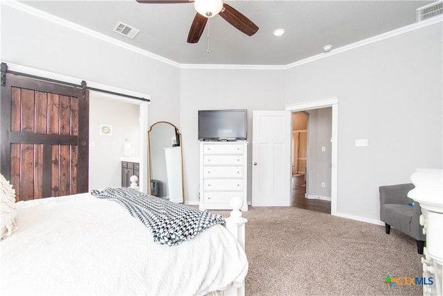 carpeted bedroom with a barn door, visible vents, baseboards, and ornamental molding