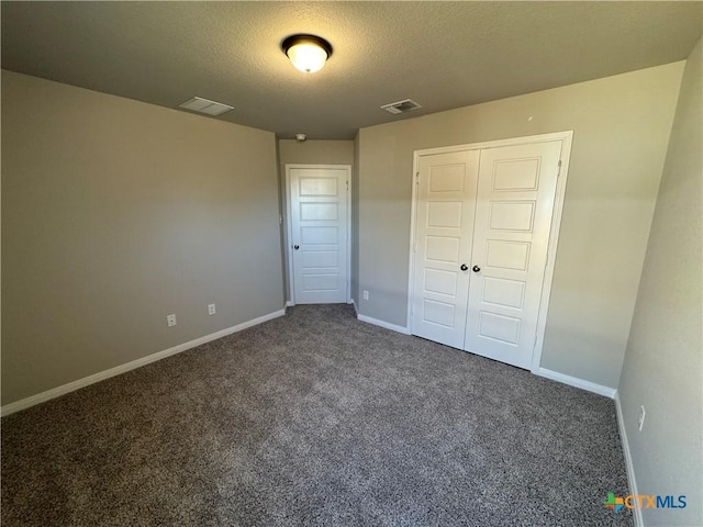 unfurnished bedroom featuring a closet, a textured ceiling, and dark colored carpet