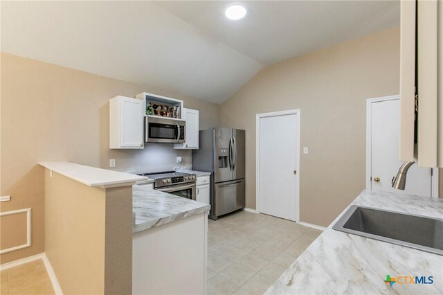 kitchen with a peninsula, lofted ceiling, white cabinets, a sink, and stainless steel appliances