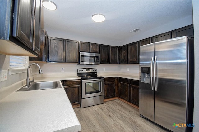 1614 Twisted Oak Dr, Temple, TX 76502 - kitchen featuring appliances with stainless steel finishes, a sink, dark brown cabinets, light wood-style flooring, and light countertops