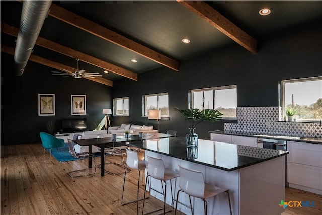 kitchen with a center island, white cabinets, lofted ceiling with beams, decorative backsplash, and light wood-type flooring