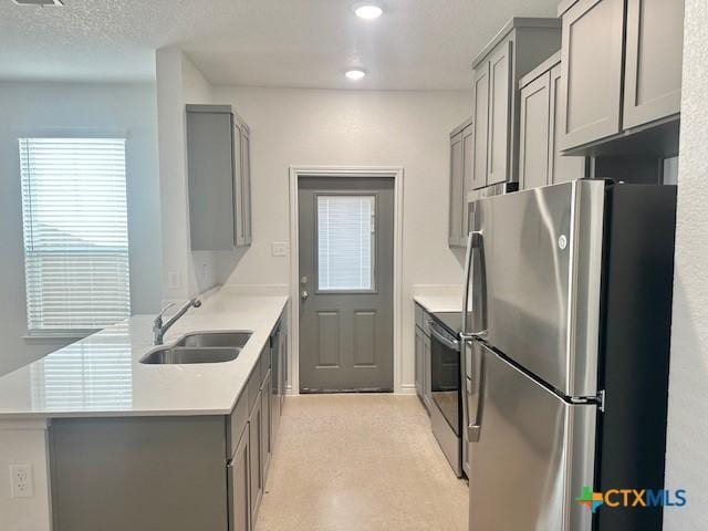 kitchen with gray cabinets, light countertops, appliances with stainless steel finishes, a sink, and a peninsula