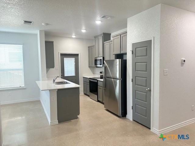 kitchen with stainless steel appliances, gray cabinets, light countertops, a sink, and a peninsula