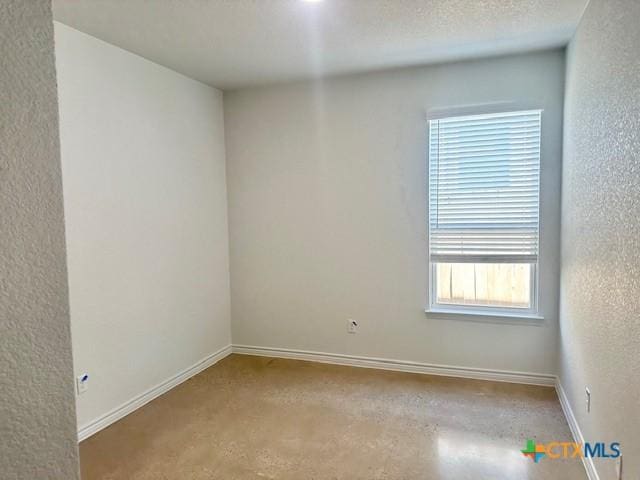 spare room with concrete flooring, a textured wall, a textured ceiling, and baseboards