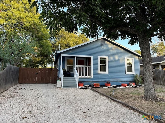 bungalow featuring covered porch, fence, and gravel driveway