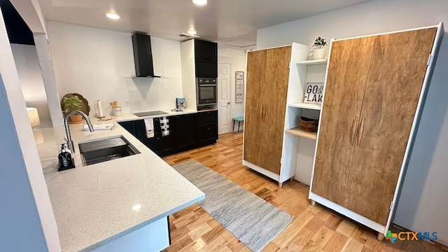 kitchen with wall chimney exhaust hood, black appliances, sink, light stone countertops, and light wood-type flooring