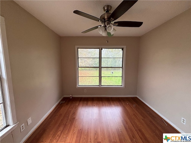 empty room with dark wood-type flooring, ceiling fan, and a healthy amount of sunlight