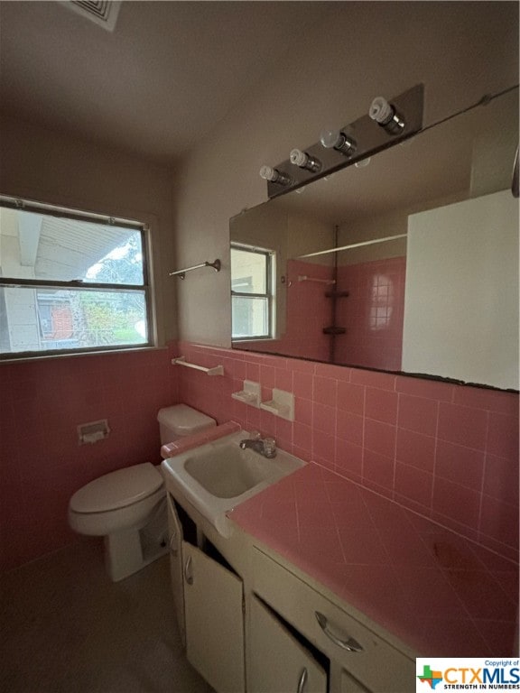 bathroom with walk in shower, vanity, toilet, and tile walls