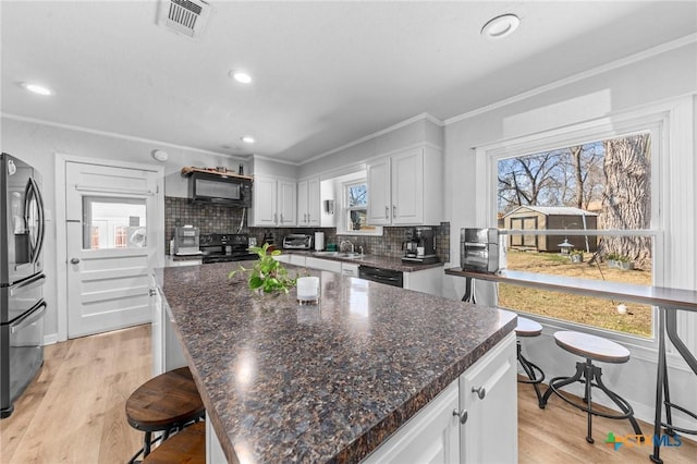 kitchen with white cabinets, decorative backsplash, a kitchen island, crown molding, and black appliances