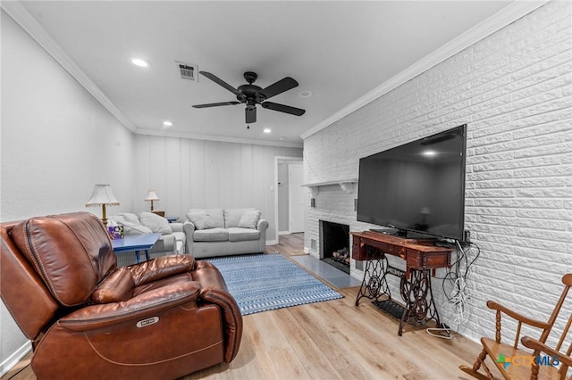 living room with crown molding, a fireplace, visible vents, ceiling fan, and light wood-type flooring