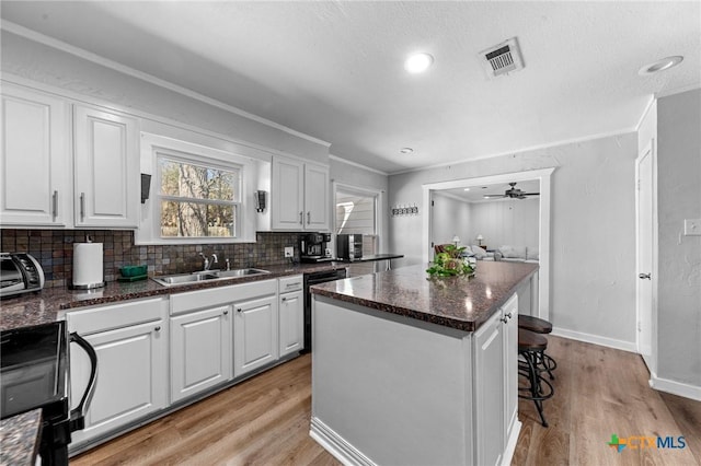 kitchen featuring visible vents, white cabinets, dishwasher, a center island, and a sink