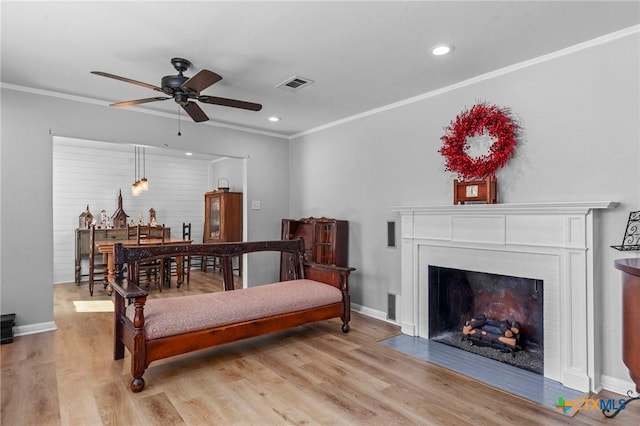 interior space featuring baseboards, visible vents, a fireplace with flush hearth, crown molding, and light wood-style floors