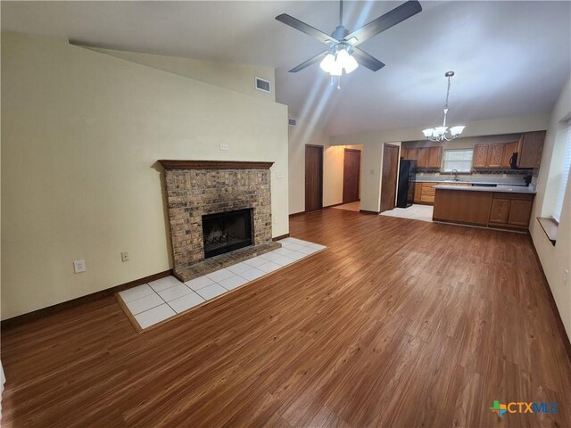 unfurnished living room featuring ceiling fan with notable chandelier, sink, vaulted ceiling, a fireplace, and light hardwood / wood-style floors