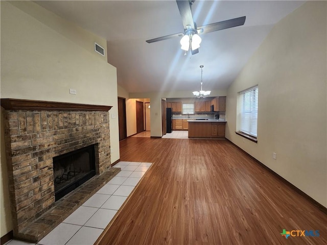 unfurnished living room with ceiling fan with notable chandelier, light wood-type flooring, a fireplace, and vaulted ceiling