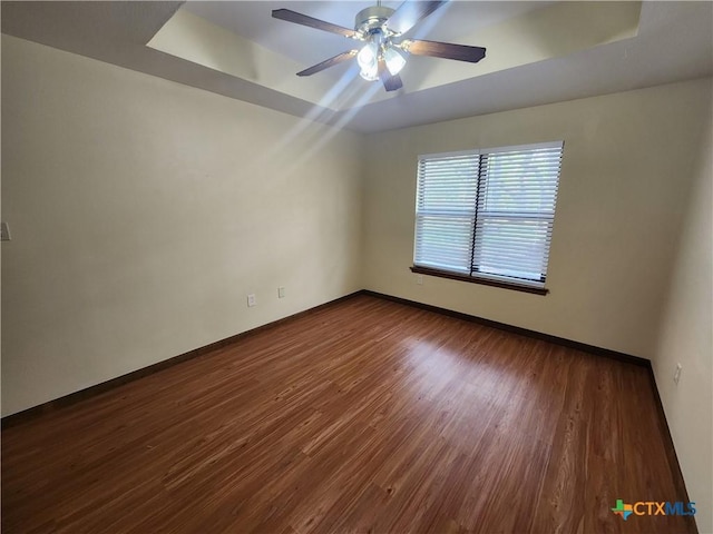 empty room with a raised ceiling, ceiling fan, and dark wood-type flooring