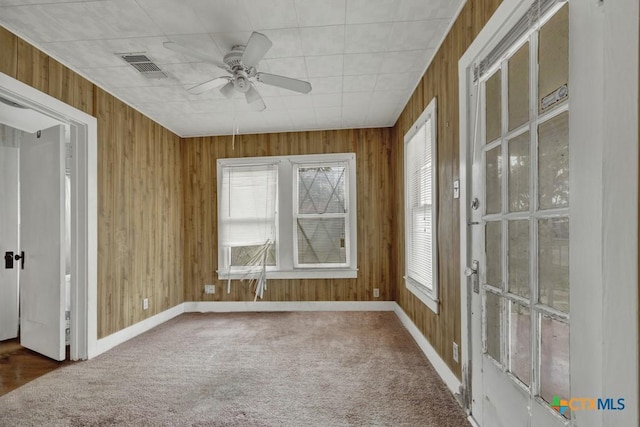 empty room with ceiling fan, wood walls, and carpet floors