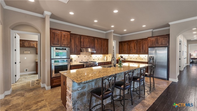 kitchen featuring appliances with stainless steel finishes, a kitchen bar, sink, dark wood-type flooring, and a kitchen island with sink