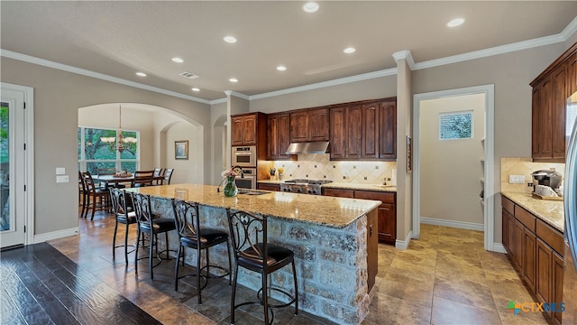 kitchen featuring ornamental molding, backsplash, stainless steel range oven, an island with sink, and wood-type flooring