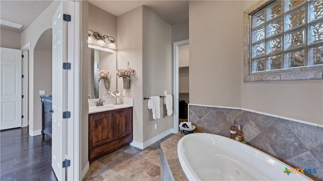 bathroom with vanity, a textured ceiling, and tiled tub