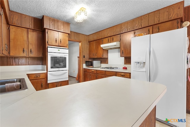kitchen featuring under cabinet range hood, light countertops, a sink, white appliances, and a warming drawer