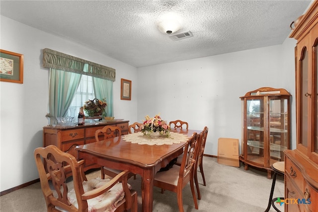 dining room featuring light carpet, a textured ceiling, visible vents, and baseboards