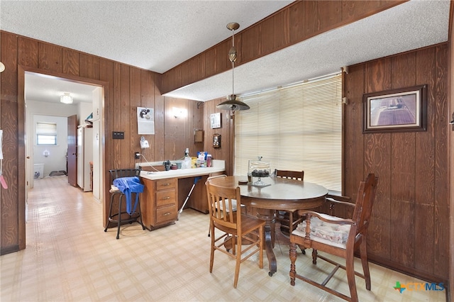 dining space featuring a textured ceiling, wood walls, and light floors