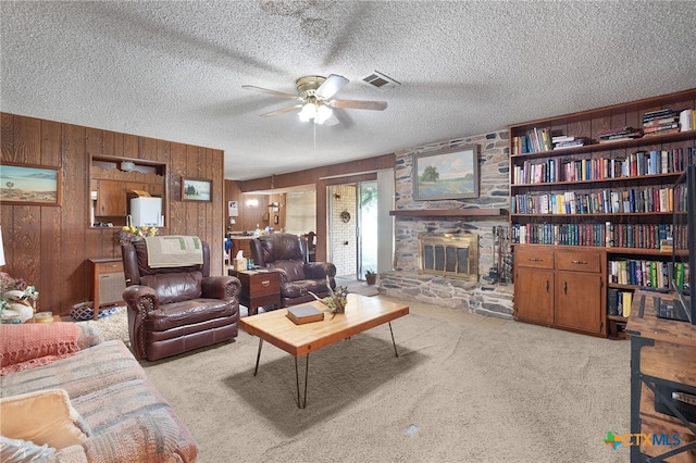 living area featuring a ceiling fan, a stone fireplace, a textured ceiling, carpet flooring, and visible vents