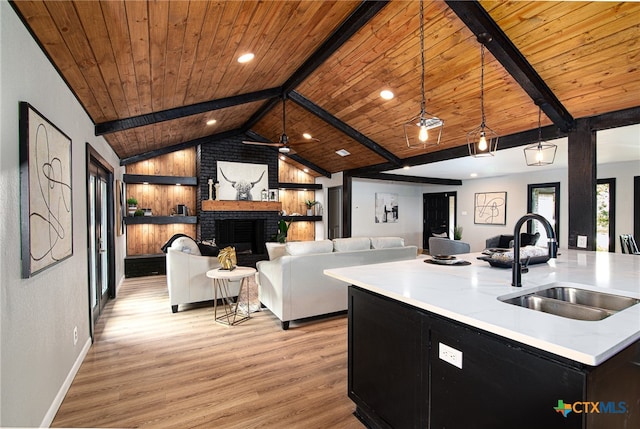 kitchen with a brick fireplace, vaulted ceiling with beams, sink, a kitchen island with sink, and pendant lighting