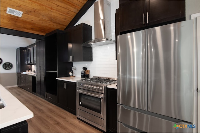 kitchen featuring stainless steel appliances, hardwood / wood-style flooring, tasteful backsplash, wall chimney exhaust hood, and vaulted ceiling