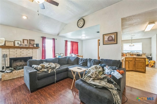 living room with a ceiling fan, a fireplace, a textured ceiling, vaulted ceiling, and wood finished floors