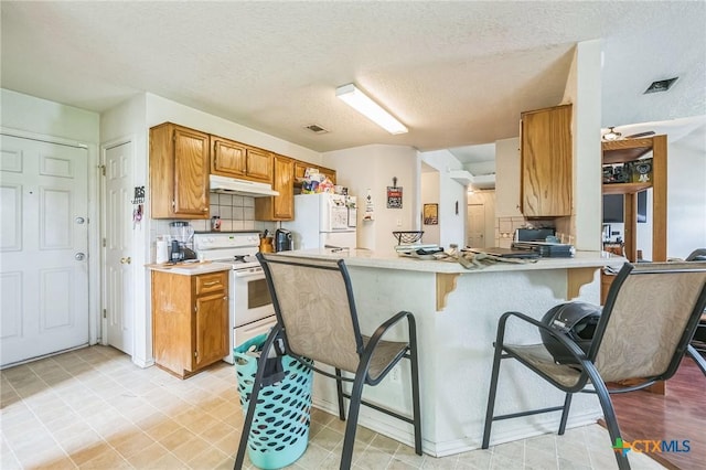 kitchen featuring white appliances, a peninsula, under cabinet range hood, light countertops, and decorative backsplash