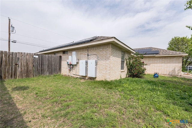 view of side of home featuring brick siding, fence, a lawn, and roof mounted solar panels