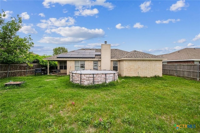 rear view of property with brick siding, a fenced backyard, a yard, and solar panels