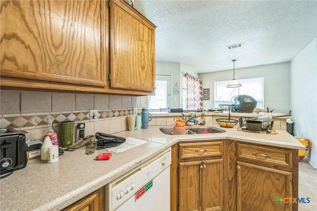 kitchen featuring a peninsula, backsplash, visible vents, dishwasher, and a sink
