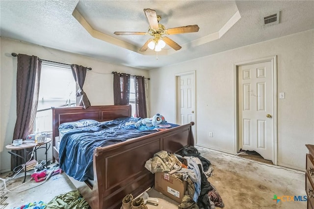 bedroom featuring a raised ceiling, a textured ceiling, ceiling fan, and visible vents