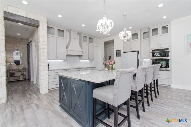 kitchen featuring tasteful backsplash, a center island with sink, hanging light fixtures, light hardwood / wood-style floors, and custom exhaust hood