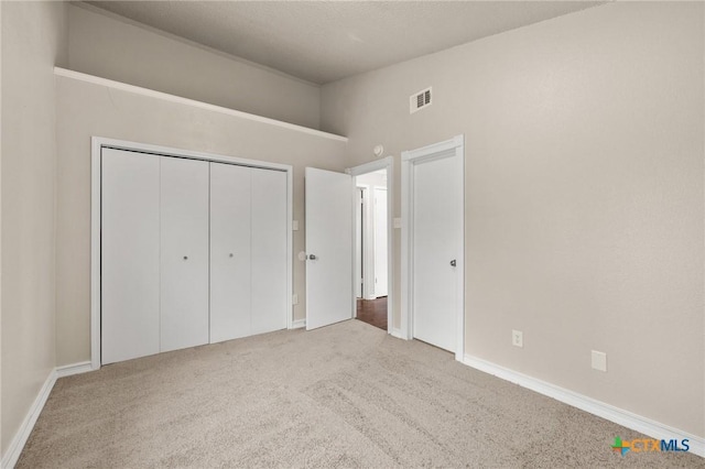 unfurnished bedroom featuring visible vents, a closet, carpet floors, baseboards, and vaulted ceiling