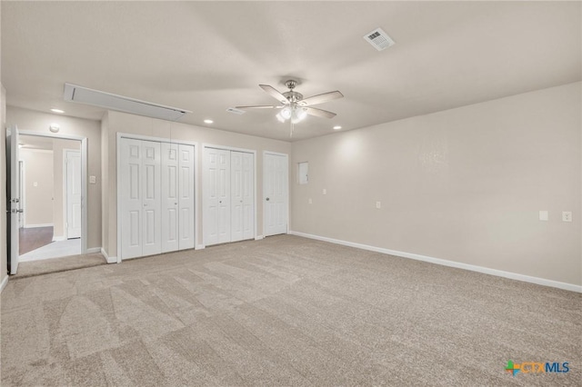 unfurnished bedroom featuring visible vents, two closets, baseboards, attic access, and carpet flooring