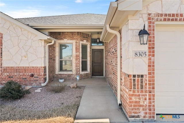 property entrance with stone siding, brick siding, roof with shingles, and an attached garage